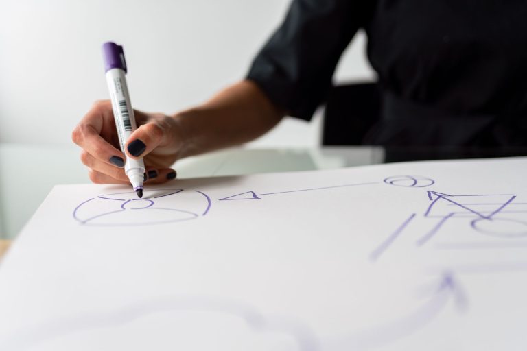 a close-up of a person's hand drawing diagrams on a large sheet of paper