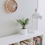 A clean and modern coffee table with a clock, a lamp, and a potted plant in a cozy room setting.