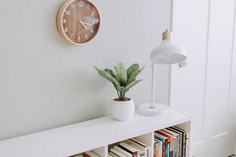 A clean and modern coffee table with a clock, a lamp, and a potted plant in a cozy room setting.